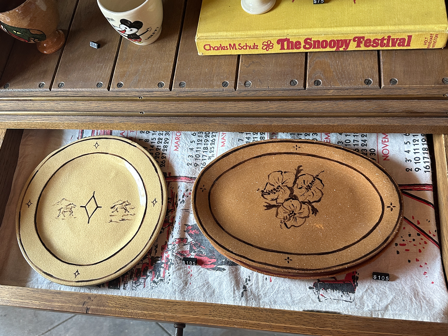 Hand-painted ceramic plates and mugs displayed on a wooden shelf