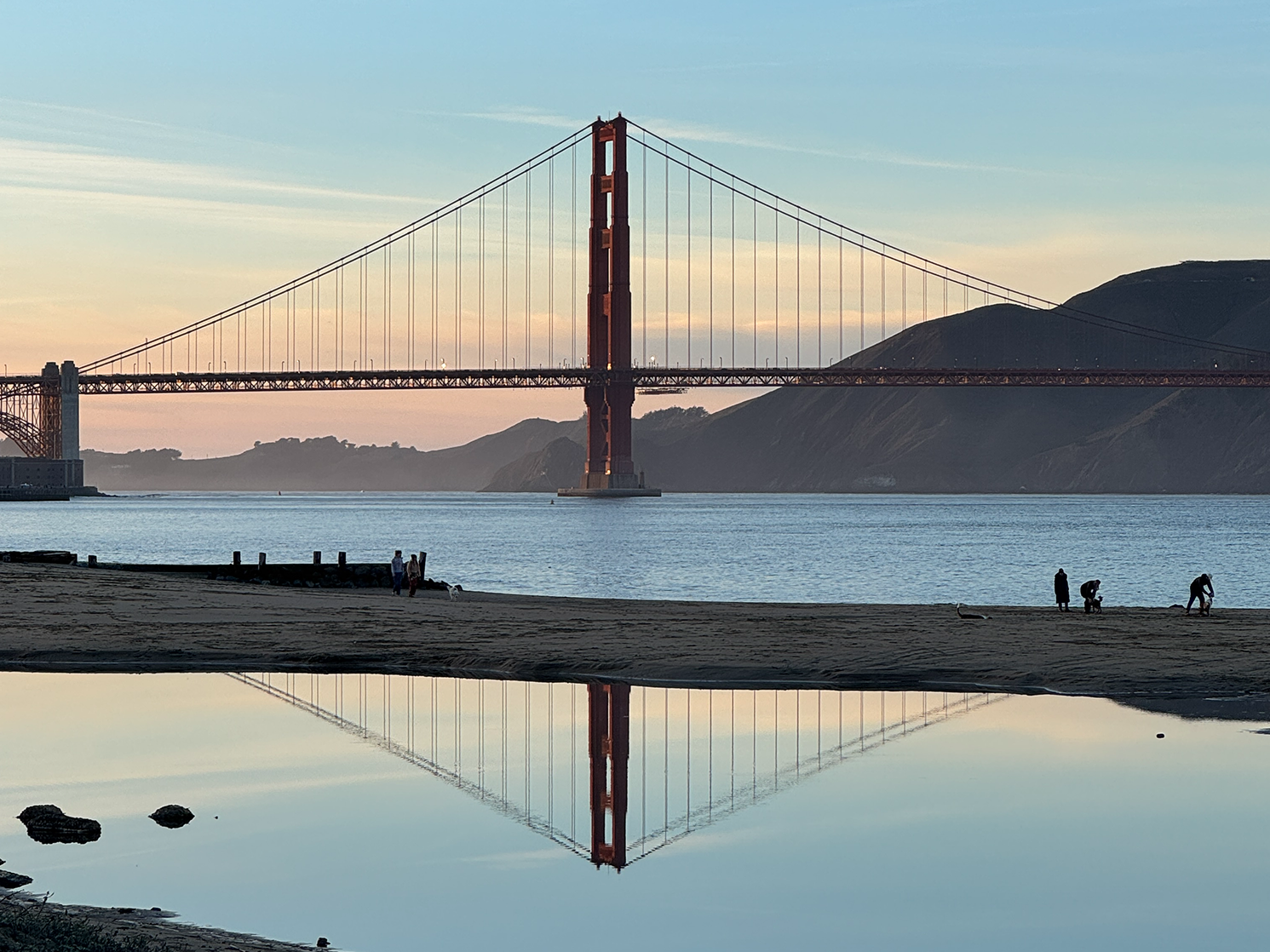 The Golden Gate Bridge at sunset, reflected in the still water of the bay